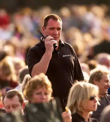 A event security guard communicates through a radio while overseeing a crowded event, ensuring safety and order.