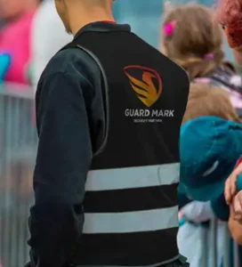 A event security guard wearing a "GUARD MARK" vest stands near a crowd, ensuring safety at an event.