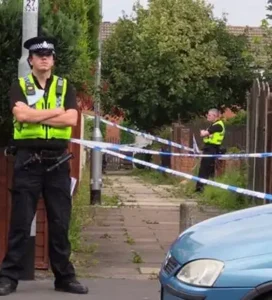 Police officers standing near a cordoned-off area in Whinmoor, indicating a potential crime scene investigation.