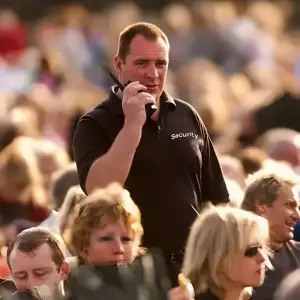 A event security guard communicates through a radio while overseeing a crowded event, ensuring safety and order.