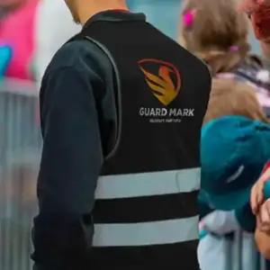 A event security guard wearing a "GUARD MARK" vest stands near a crowd, ensuring safety at an event.